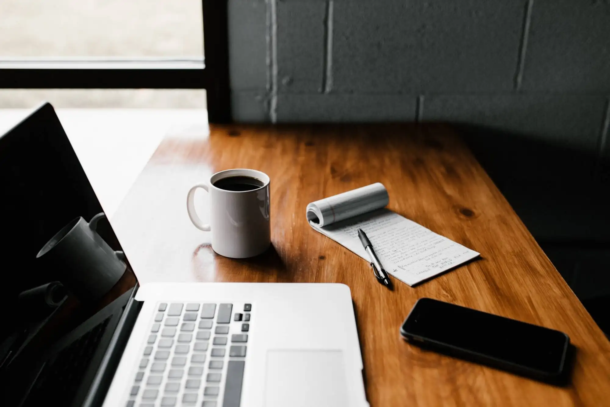 mug of coffee, notepad, laptop and phone on a desk